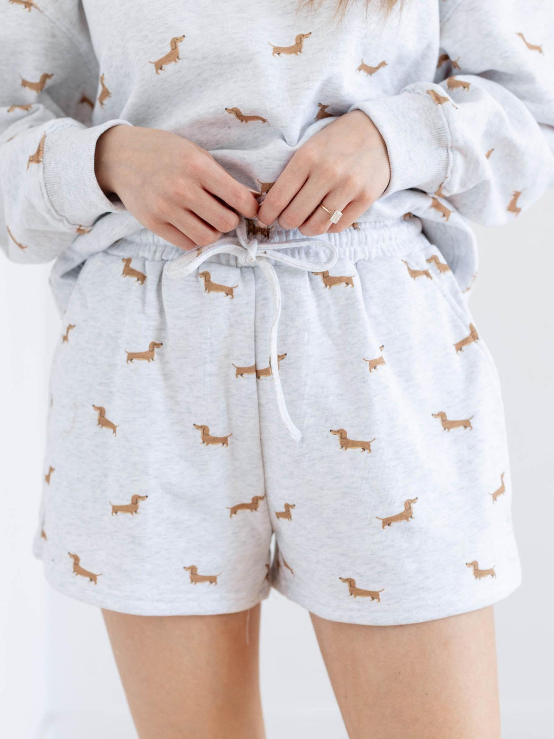 Person wearing a light gray pajama set with dachshund patterns on a white background
