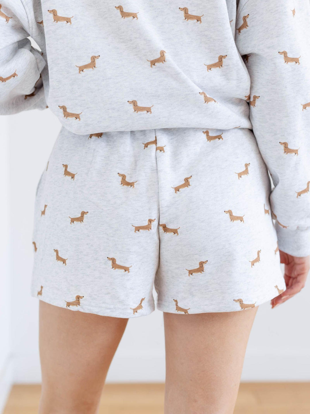 Person wearing a light gray pajama set with dachshund patterns on a white background