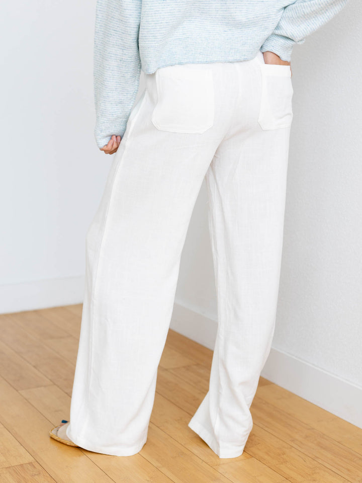 Person wearing light blue sweater and white pants on a wooden floor with white walls.