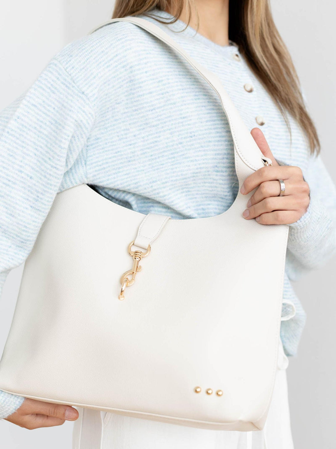 Person holding a beige handbag with a gold clasp against a neutral background