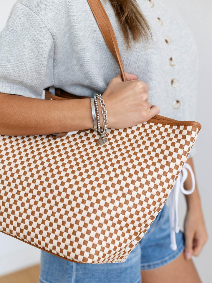 Person holding a brown and white checkered bag with a neutral background