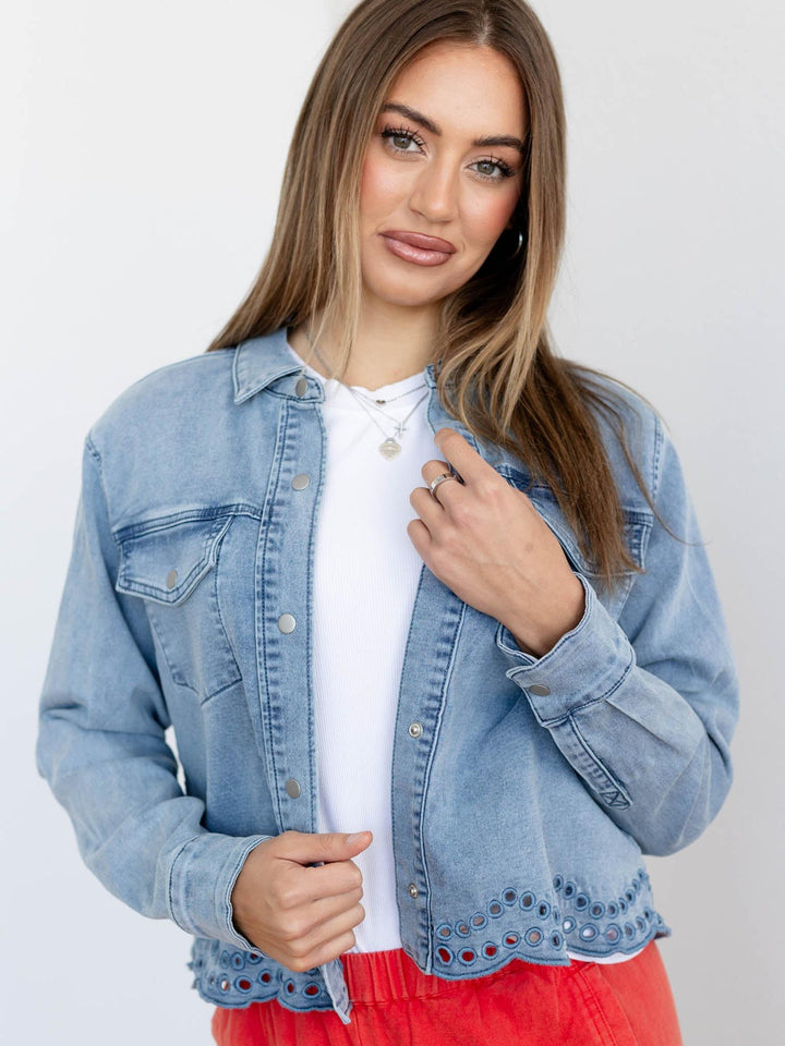 Woman wearing a light blue denim jacket over a white shirt with a red skirt on a plain background