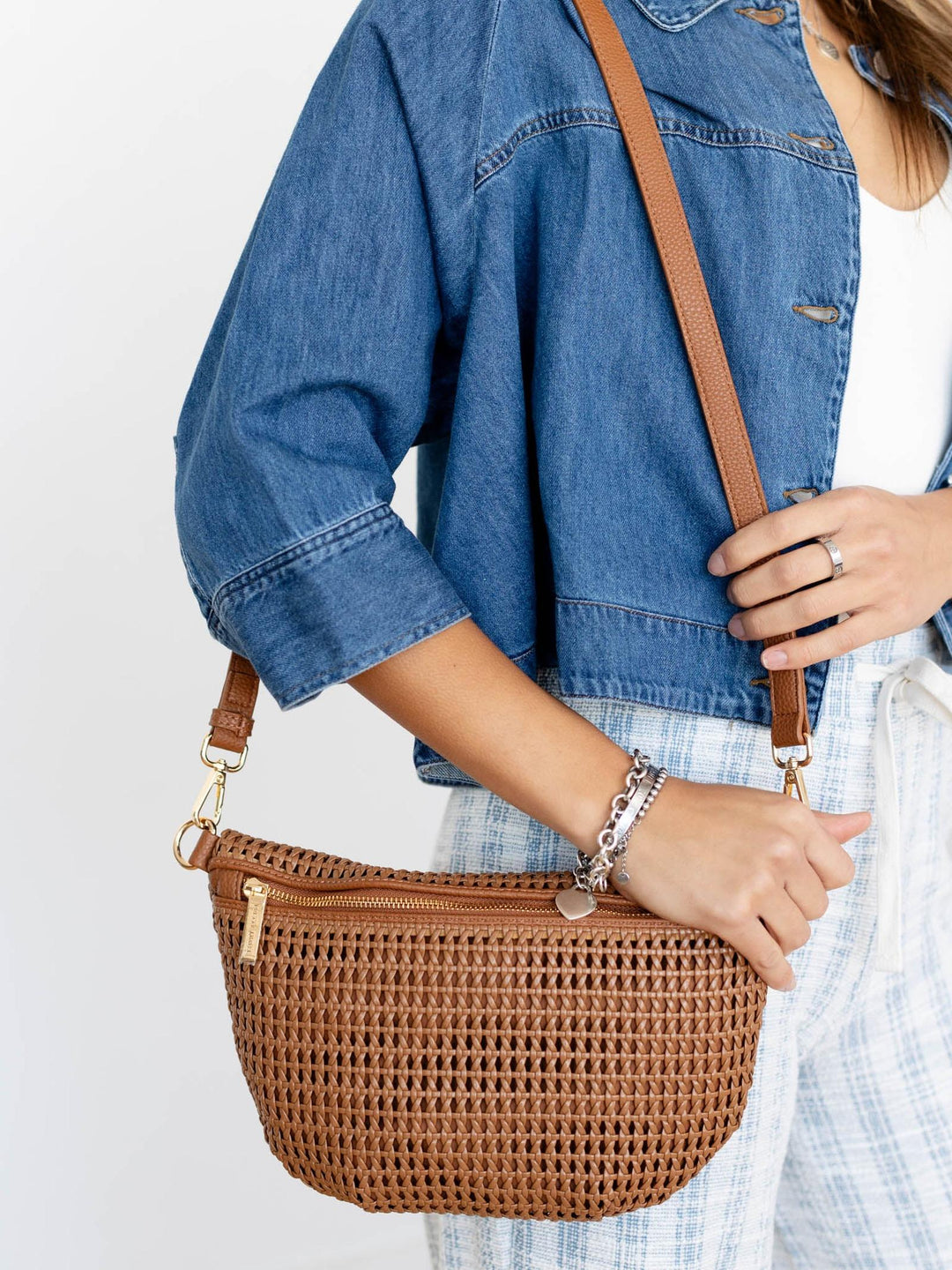 Person holding a brown woven handbag with a plain background