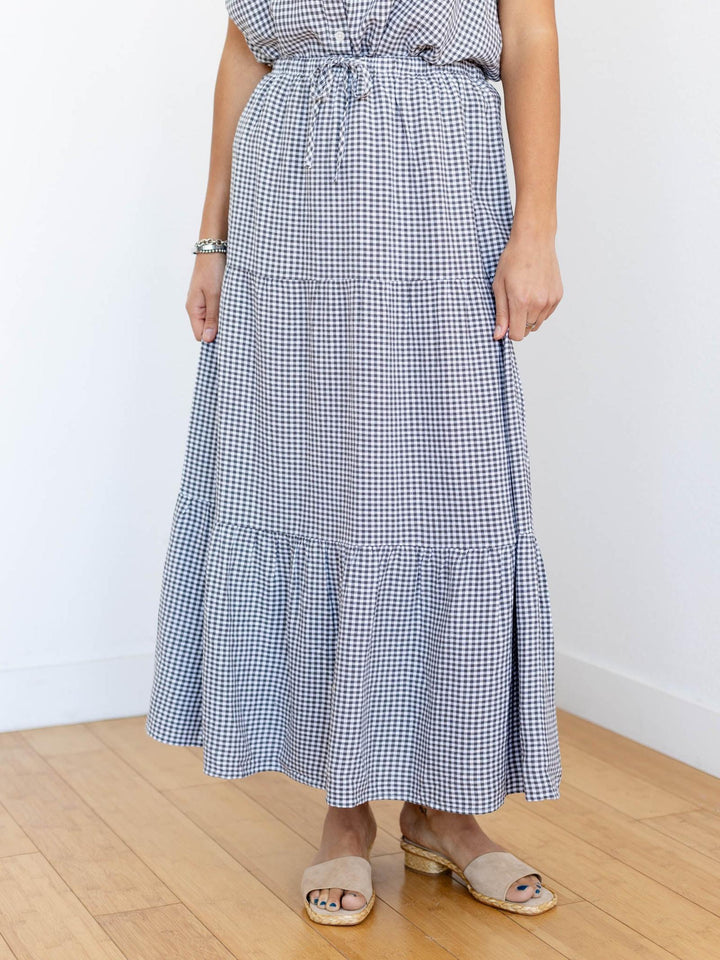 Person wearing a blue and white checkered dress on a wooden floor with a white wall background