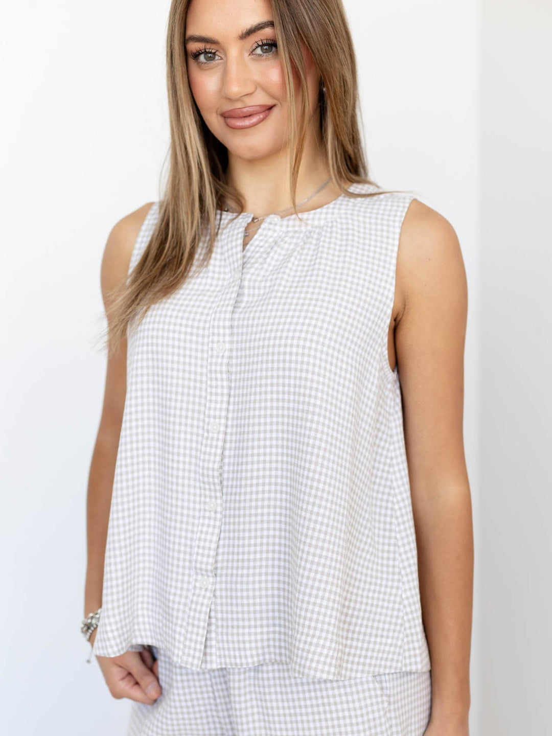 Woman wearing a sleeveless white checkered top on a plain background