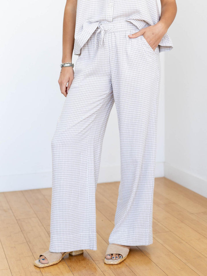 Person wearing a checkered outfit with wide-leg pants on a wooden floor.