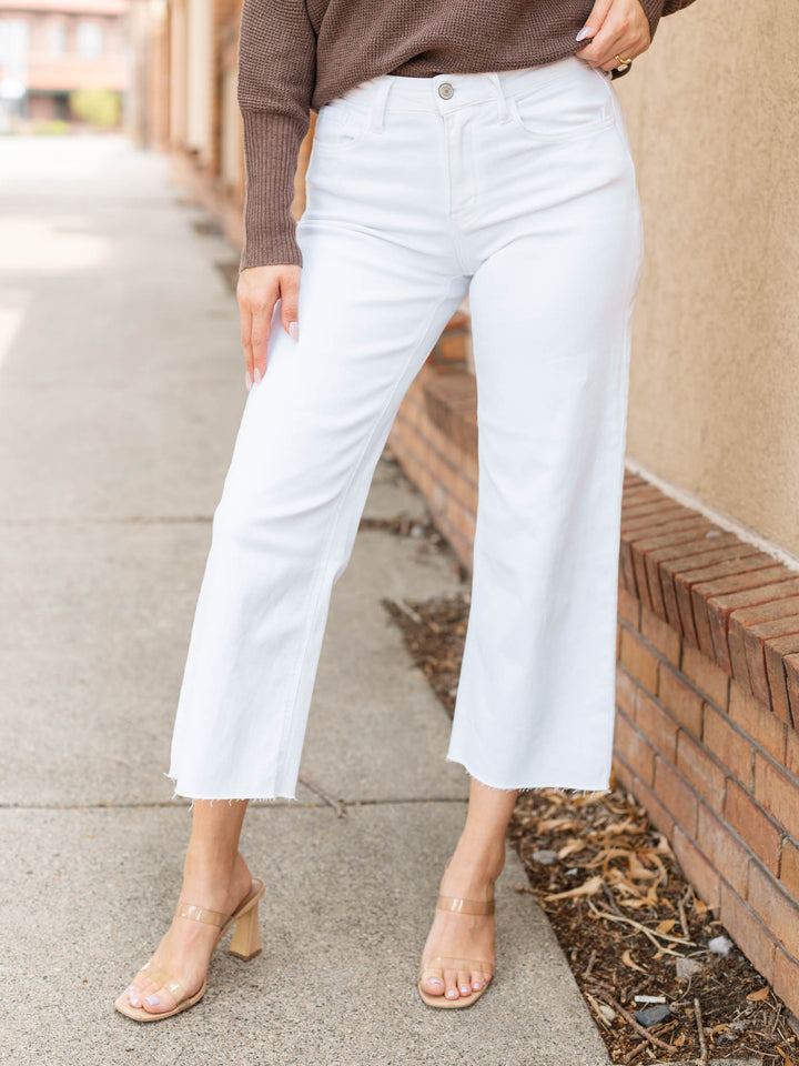 White cropped wide-leg jeans worn by a model standing outdoors on a sidewalk next to a brick wall.