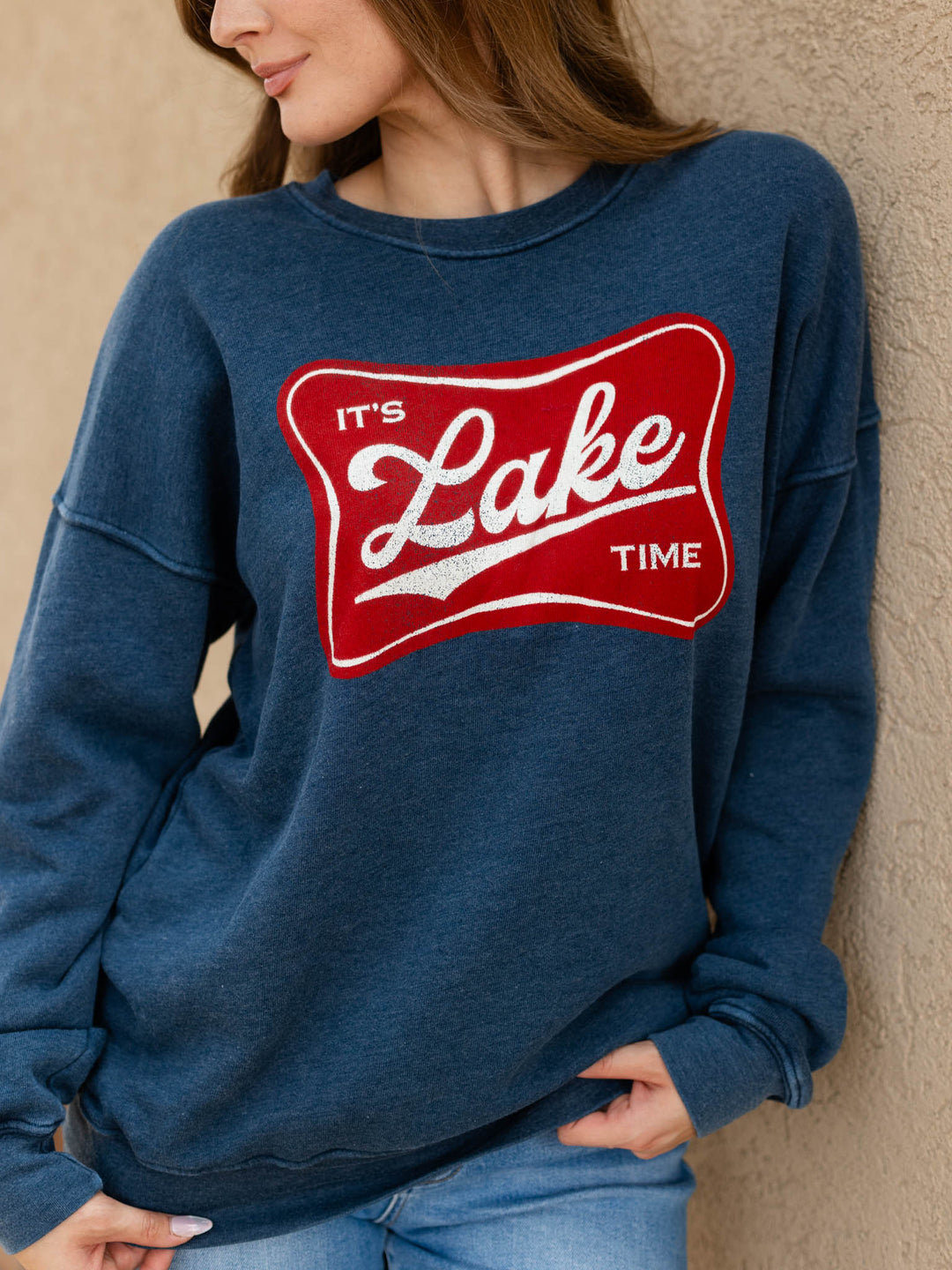 A woman wearing a heathered navy blue crewneck sweatshirt with a red and white graphic that reads &