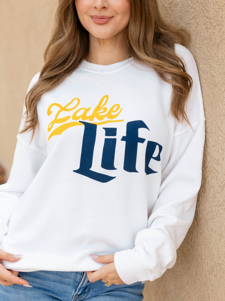 A woman wearing a white crewneck sweatshirt with a graphic that reads &