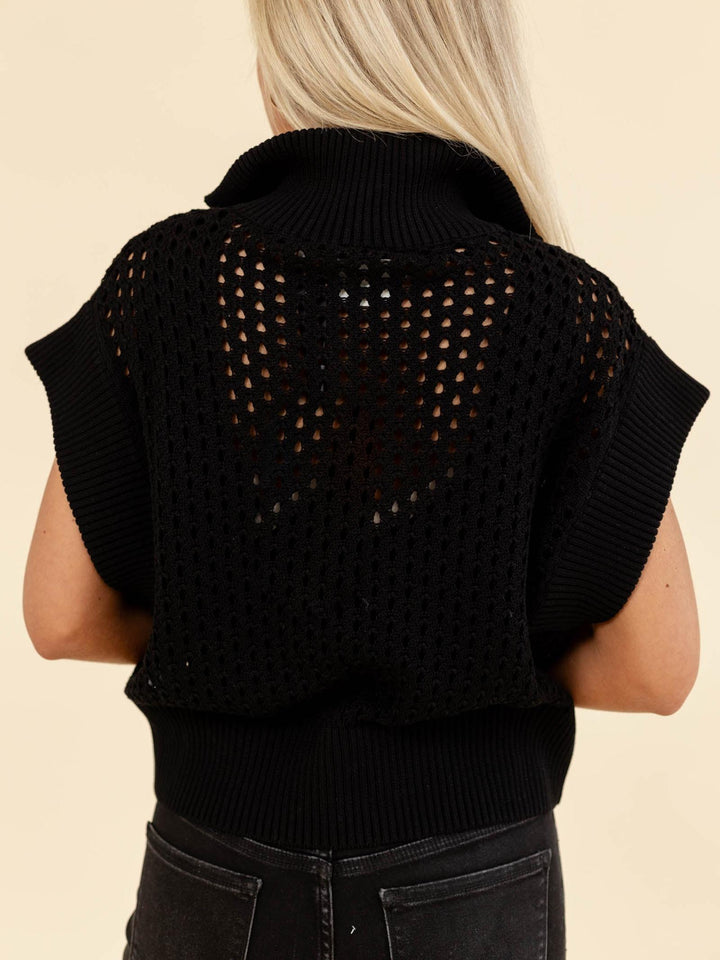 Black knitted vest worn by a person on a beige background