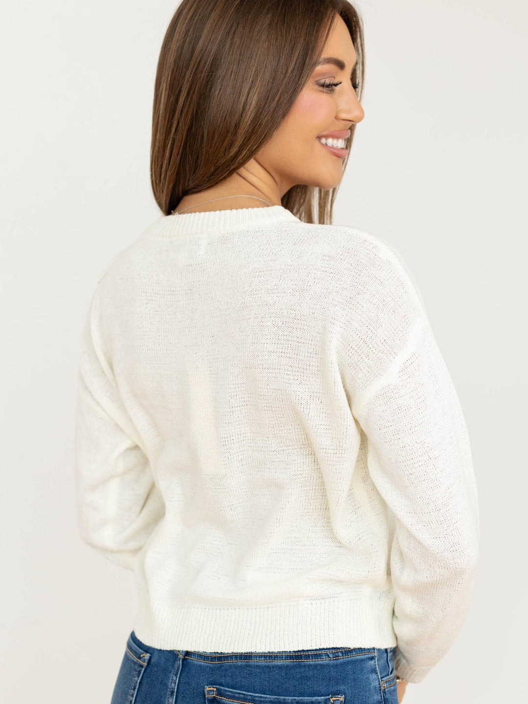 Woman wearing a white sweater and blue jeans on a plain background