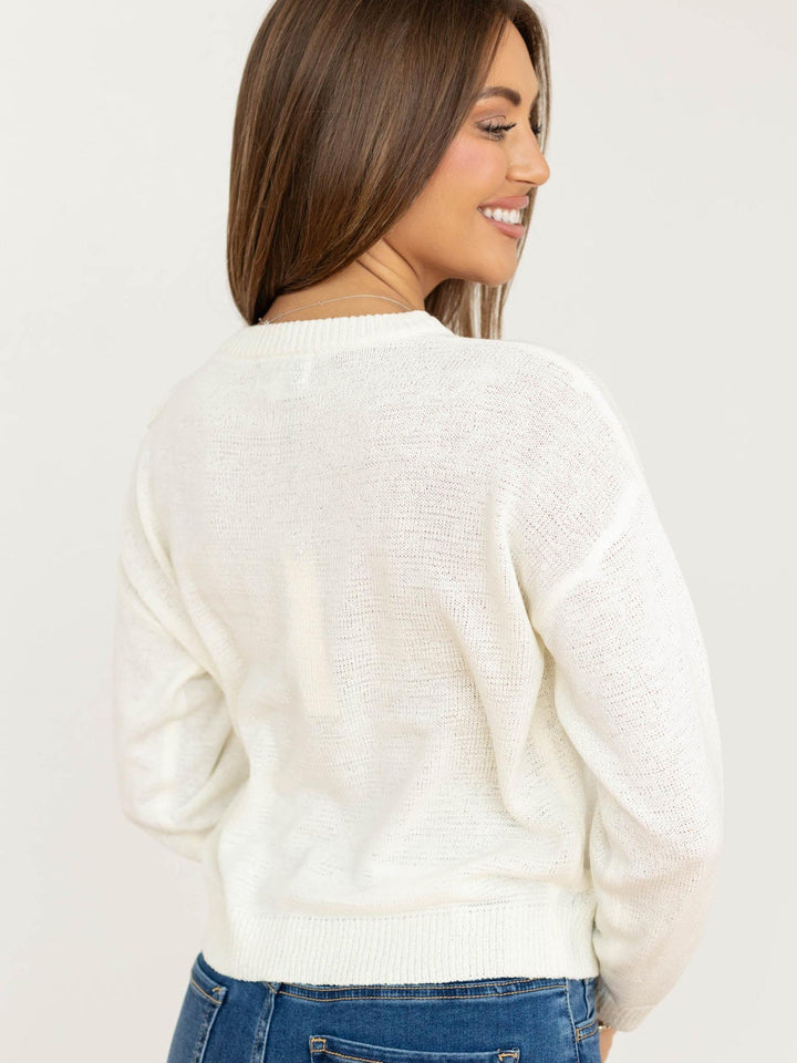 Woman wearing a white sweater and blue jeans on a plain background