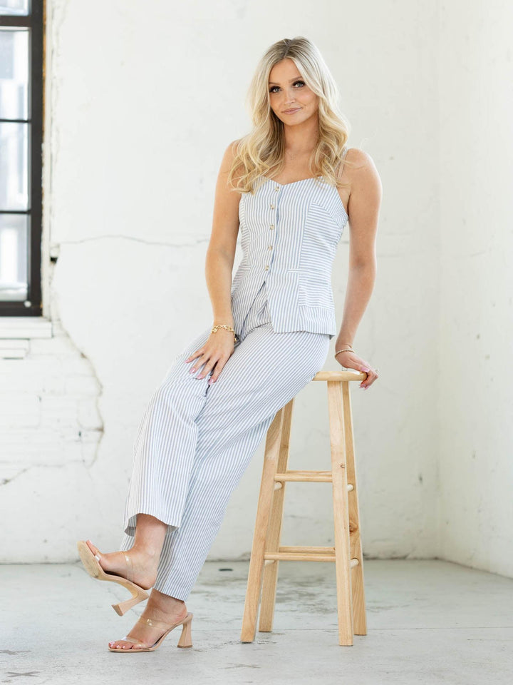 Woman sitting on a wooden stool wearing a light blue striped outfit in a bright room.