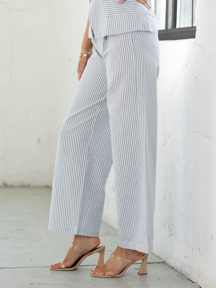 Person wearing a white and gray striped outfit with high-waisted pants in a minimalistic setting.