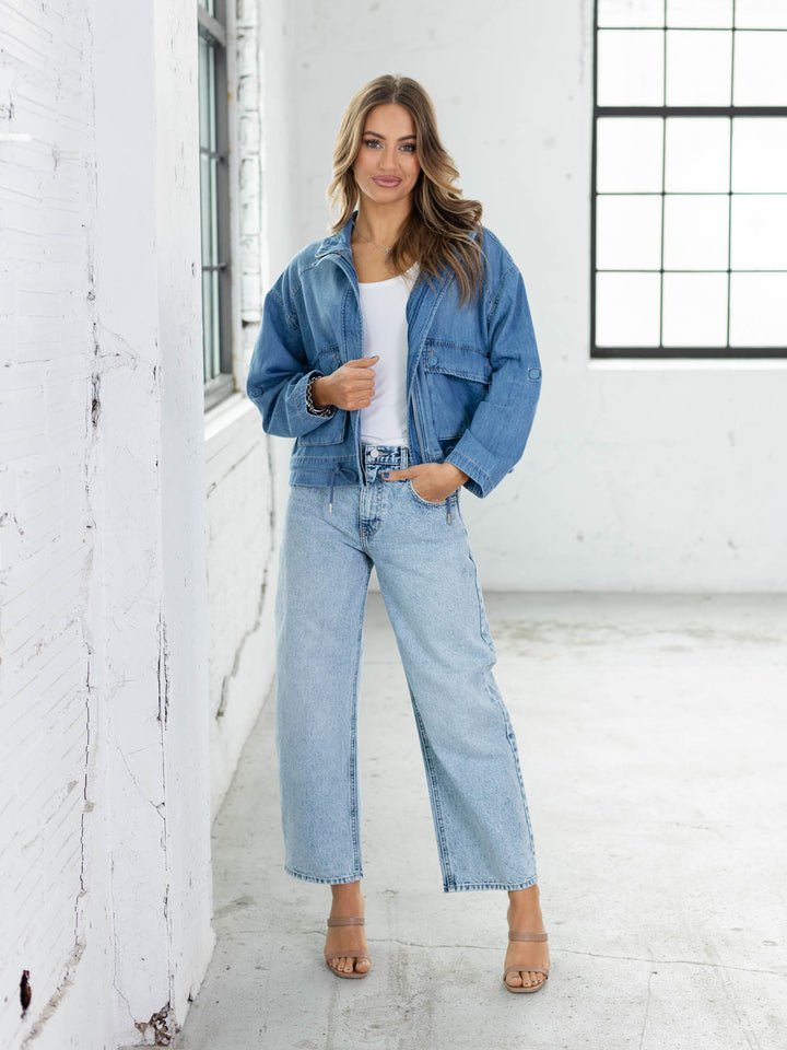 Woman wearing a denim jacket and jeans in a white room