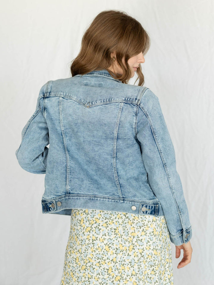 Person wearing a light blue denim jacket on a white background