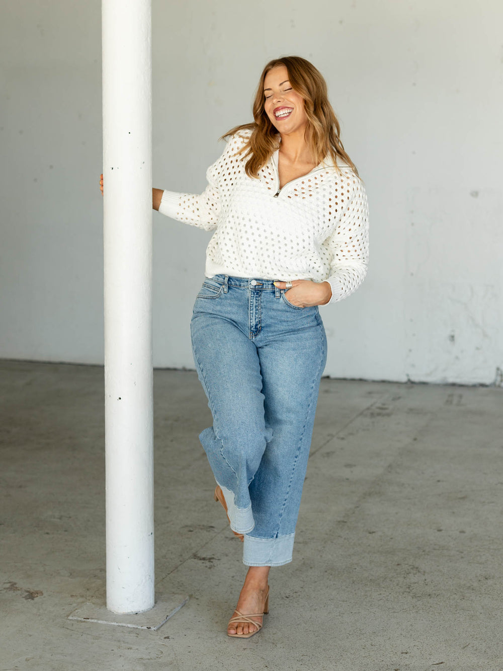 Woman wearing a white blouse and blue jeans standing against a white wall.