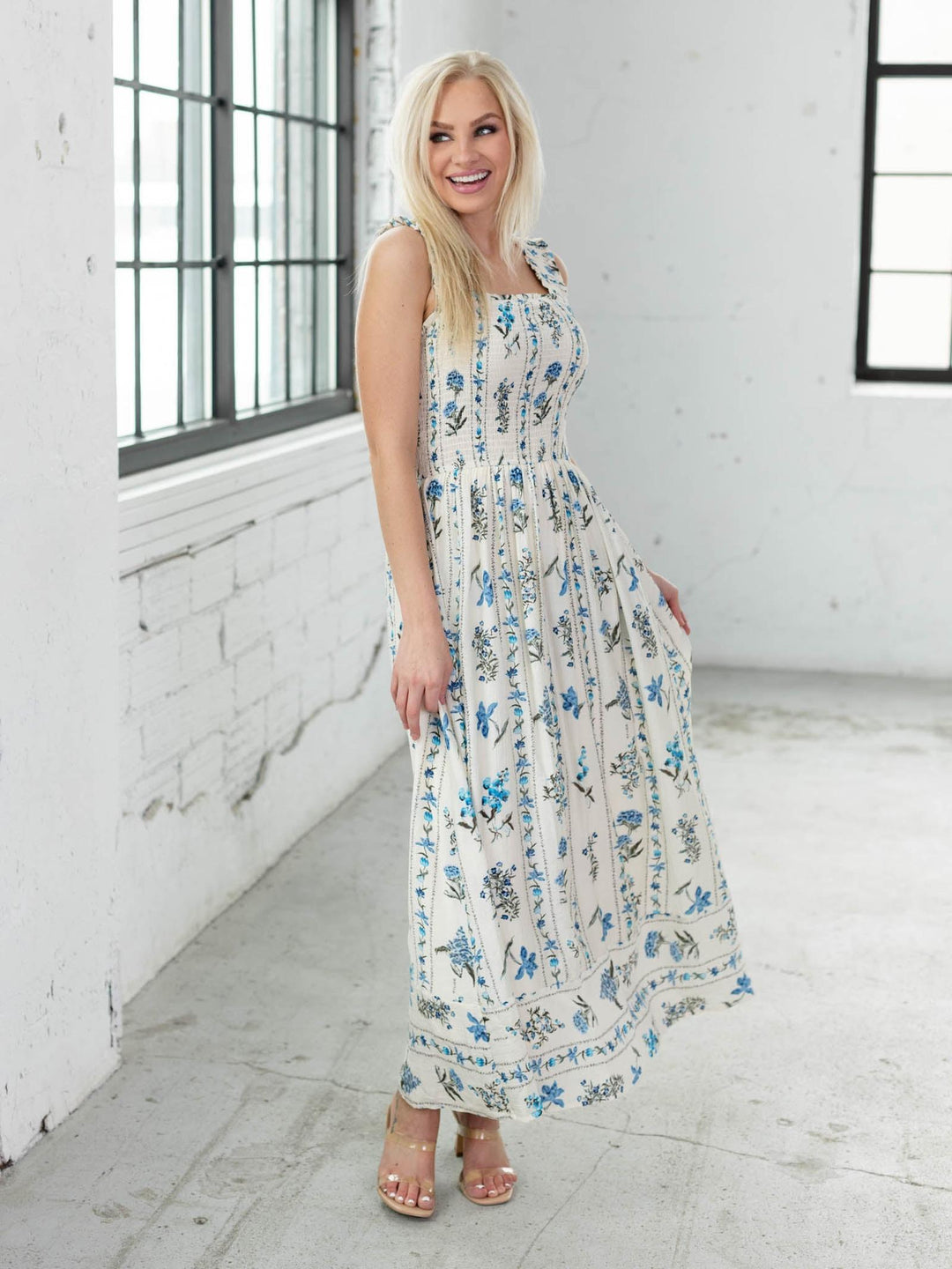 Woman wearing a floral dress in a bright room with large windows.