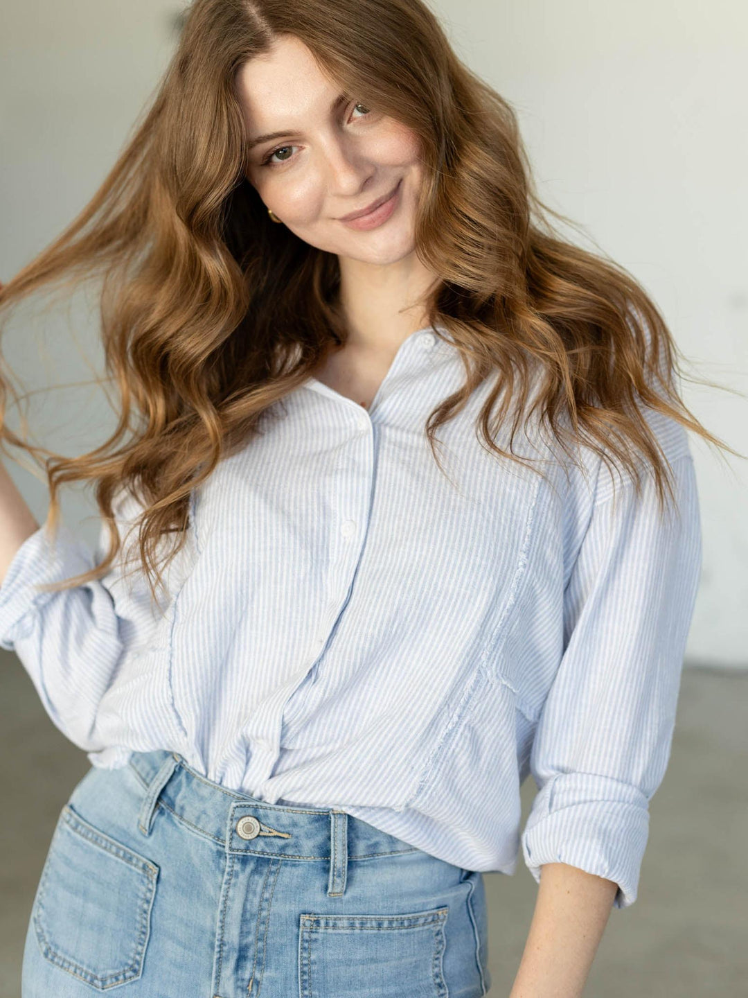Woman wearing a light blue striped shirt and jeans with a neutral background