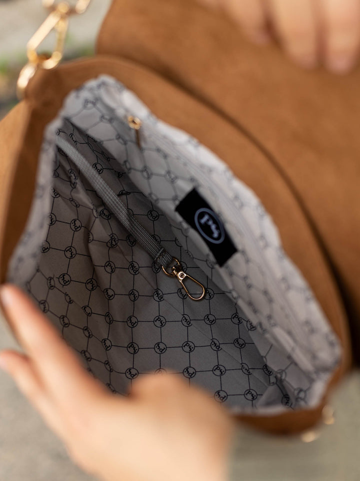 Close-up of the interior of a brown handbag with a gray patterned lining and gold-tone hardware, held open by hands.