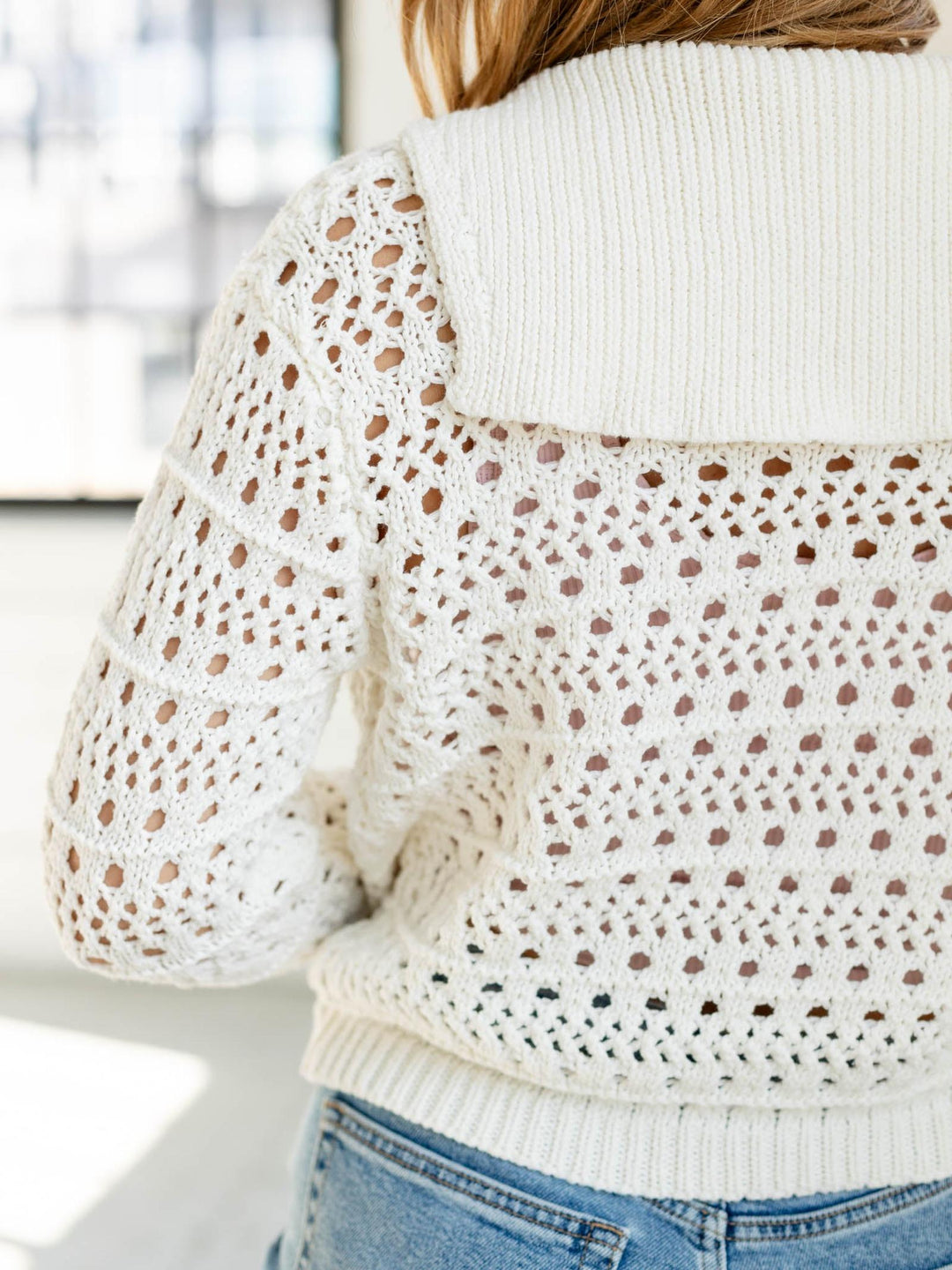 Close-up of a person wearing a white sweater with a brown polka dot pattern over a blue shirt.