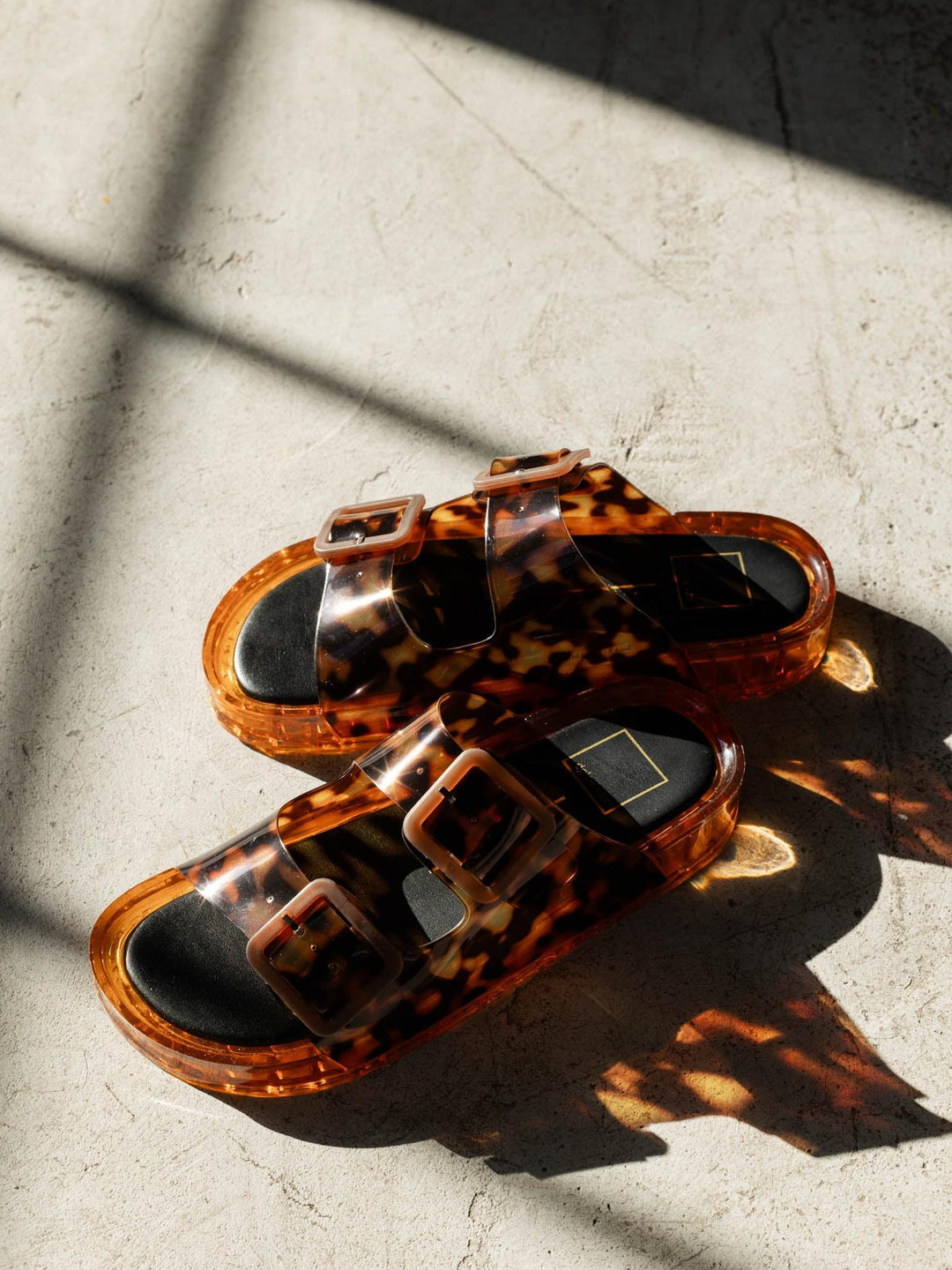 Tortoiseshell sandals on a textured surface with shadows