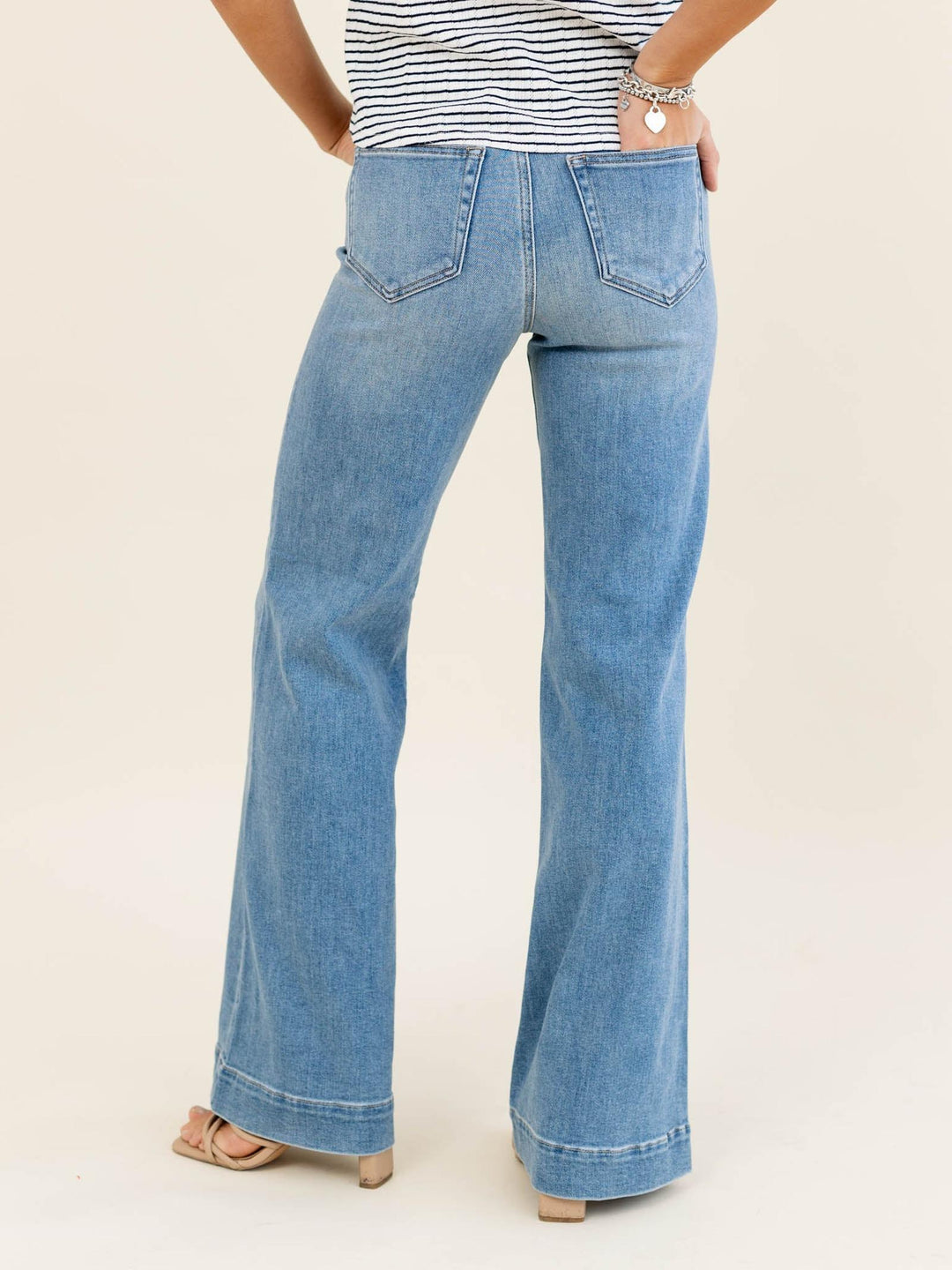 Person wearing blue flared jeans and a striped shirt on a beige background