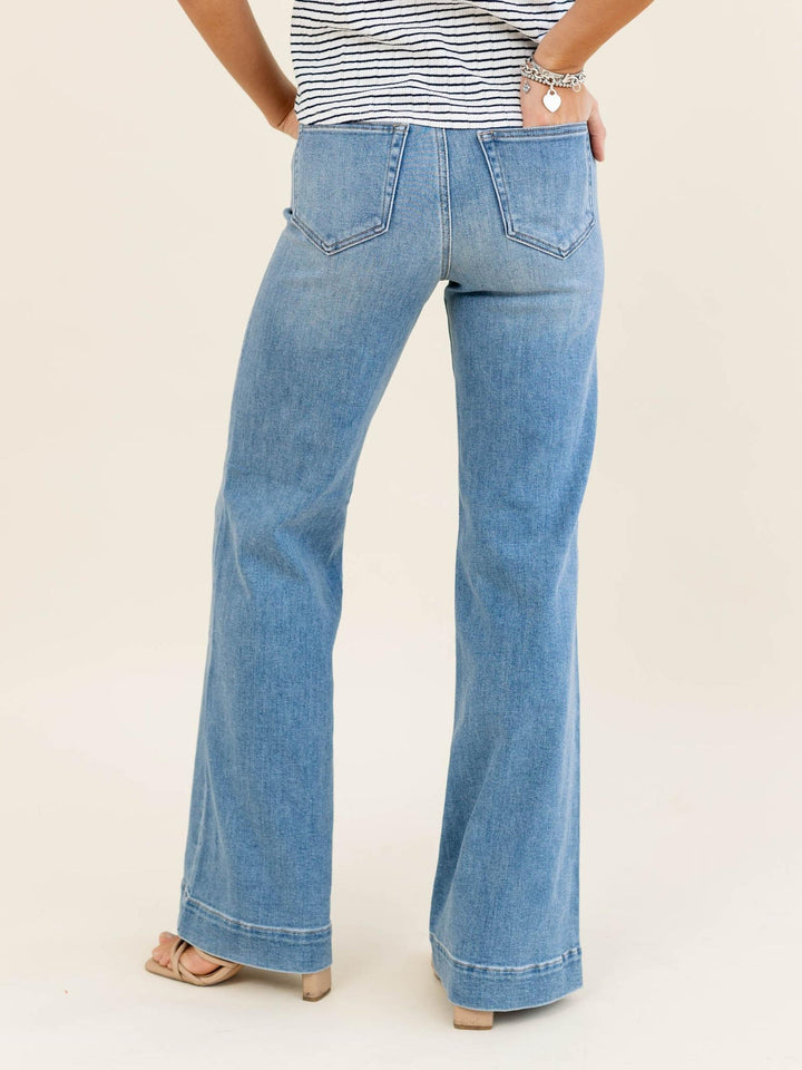 Person wearing blue flared jeans and a striped shirt on a beige background