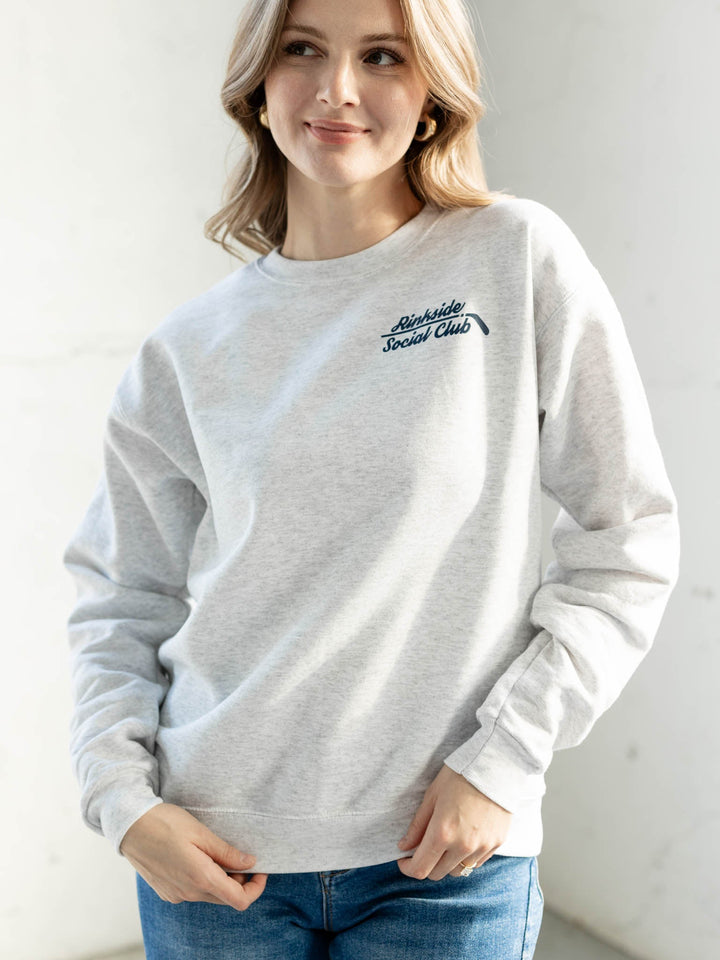 Woman wearing a light gray sweatshirt with a logo on a plain background