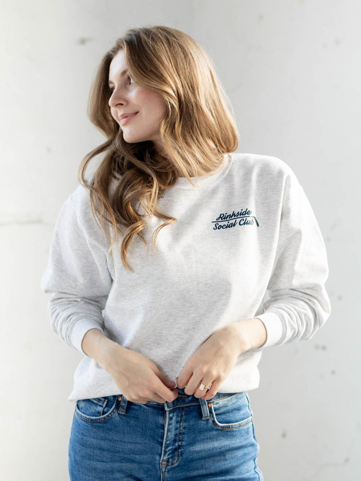 Woman wearing a white sweatshirt with text and blue jeans against a light background