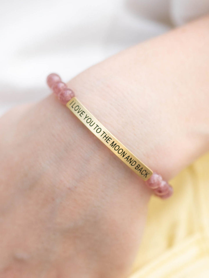 Pink Quartz stone bracelet with a gold bar engraved "I Love You To The Moon And Back" on a wrist.
