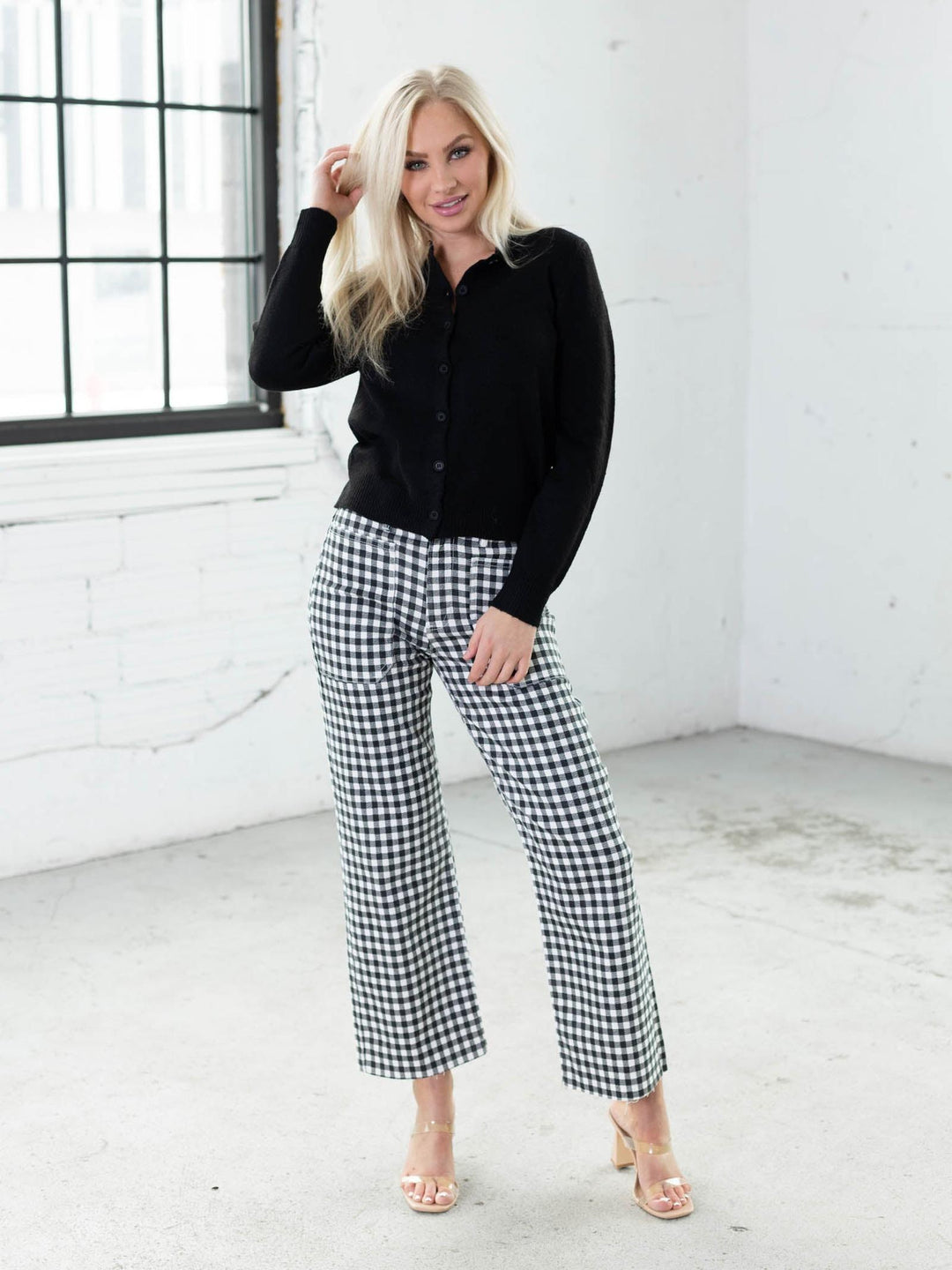 Woman wearing a black top and gingham pants in a bright room.
