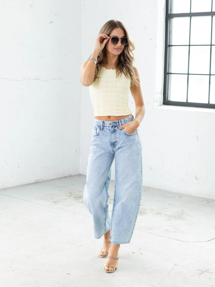 Woman wearing a yellow top and light blue jeans in a bright room.
