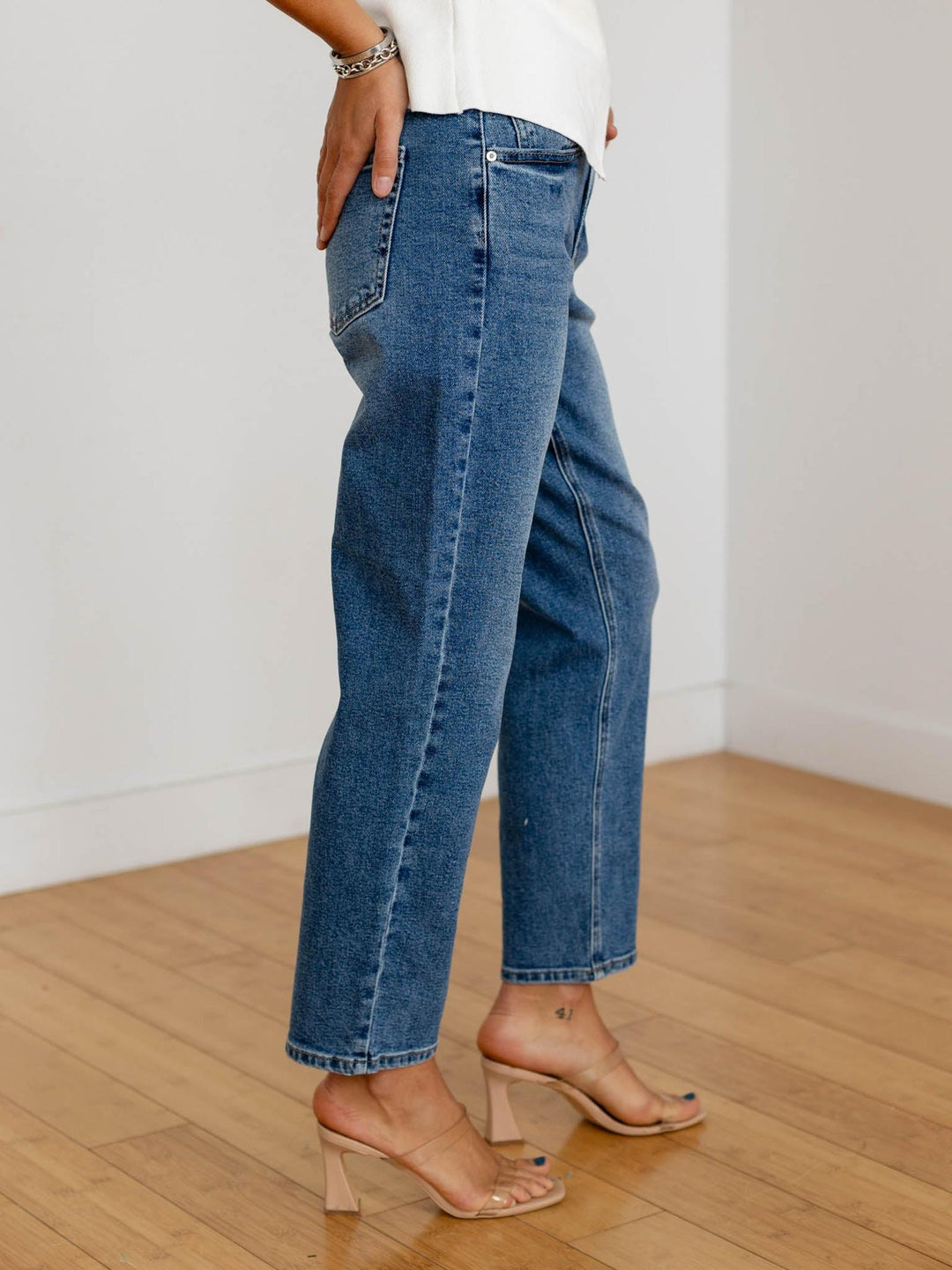 Person wearing blue jeans and a white top on a wooden floor with a white wall background