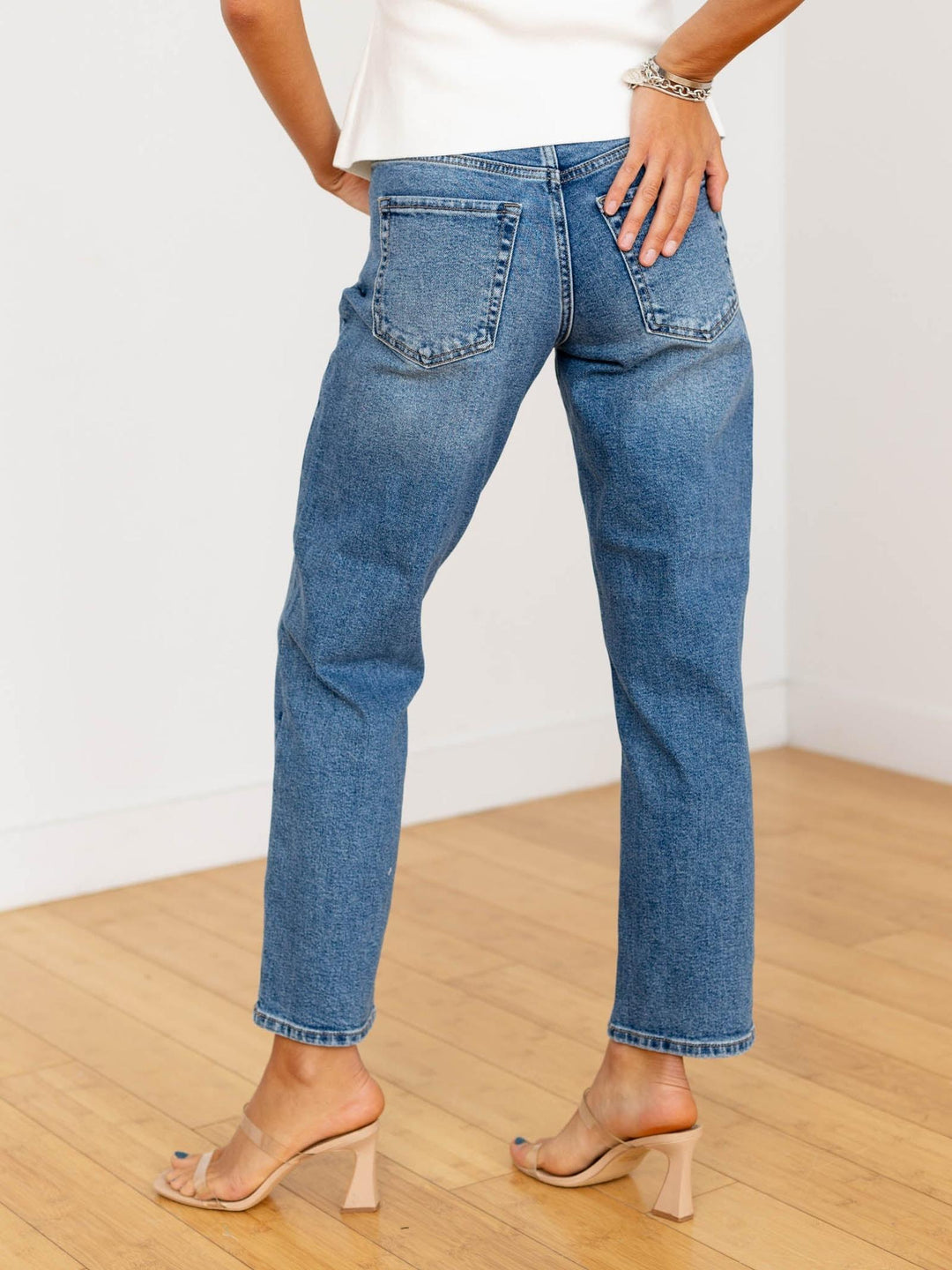 Person wearing blue jeans and a white top on a wooden floor with a white wall background