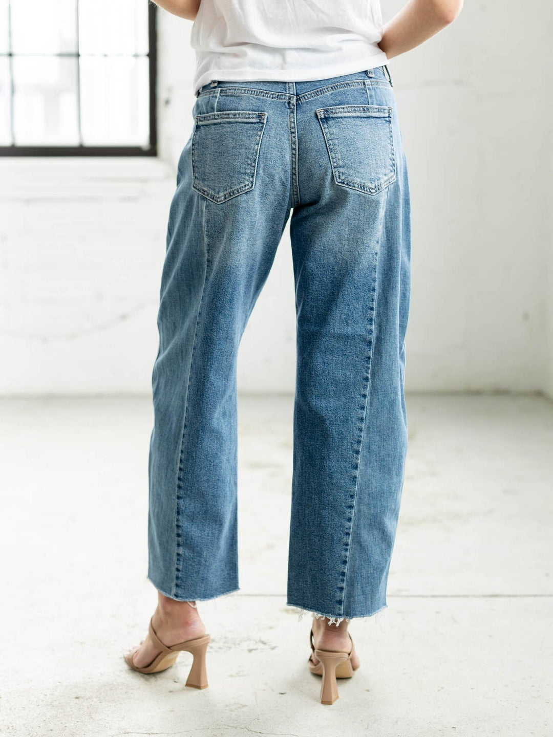 Woman wearing a white t-shirt and blue jeans standing in a minimalistic room.