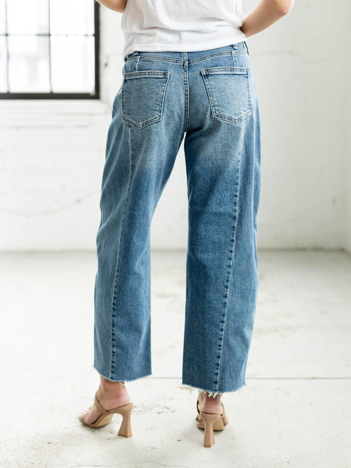 Woman wearing a white t-shirt and blue jeans standing in a minimalistic room.