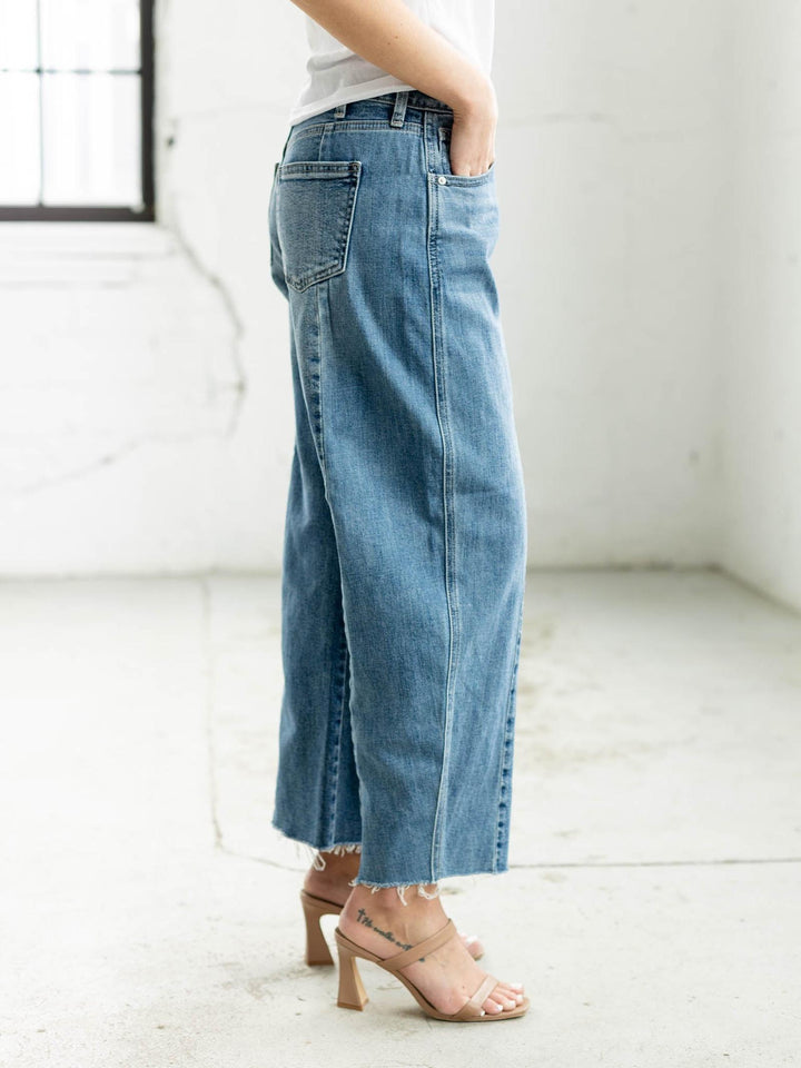 Woman wearing a white t-shirt and blue jeans standing in a minimalistic room.
