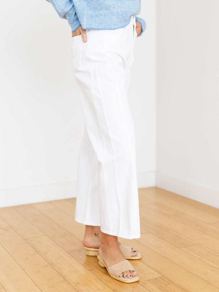 Person wearing white pants and a light blue sweater in a minimal indoor setting
