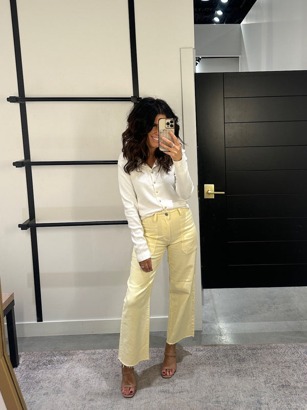 Person taking a mirror selfie wearing a white shirt and yellow pants in a room with a black door and ladder.