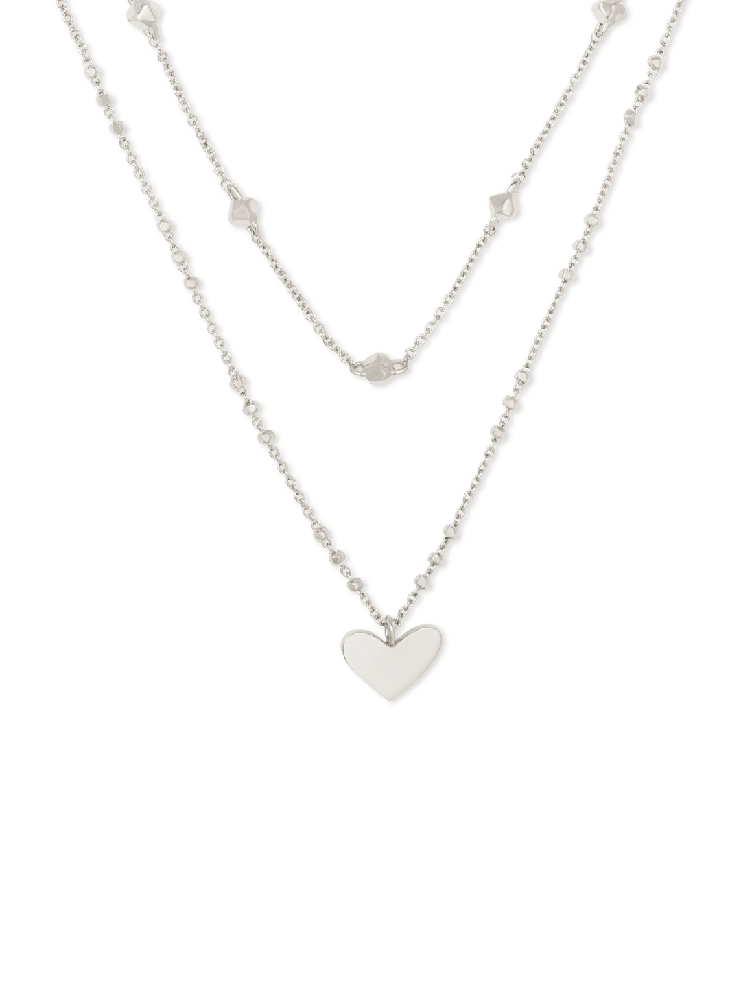 A silver double-layered necklace featuring a delicate chain with small star-shaped charms and a longer chain with a polished heart pendant, displayed against a solid white background.