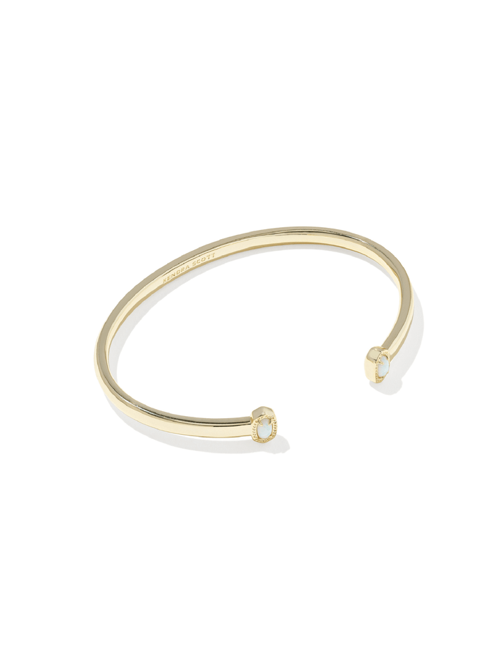 A slim gold-tone open cuff bangle bracelet with a small oval clear stone set in each end, shown on a clean white background.