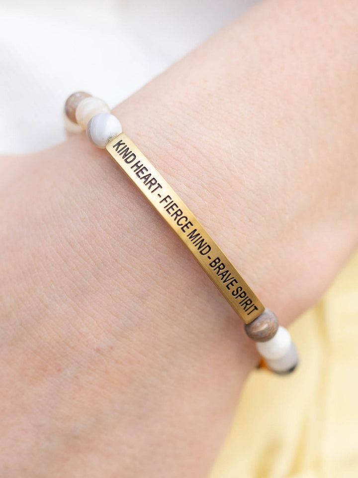 Gold bar bracelet with "KIND HEART - FIERCE MIND - BRAVE SPIRIT" text, flanked by natural stone beads.