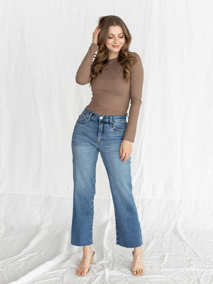 Woman wearing a brown top and blue jeans against a white background