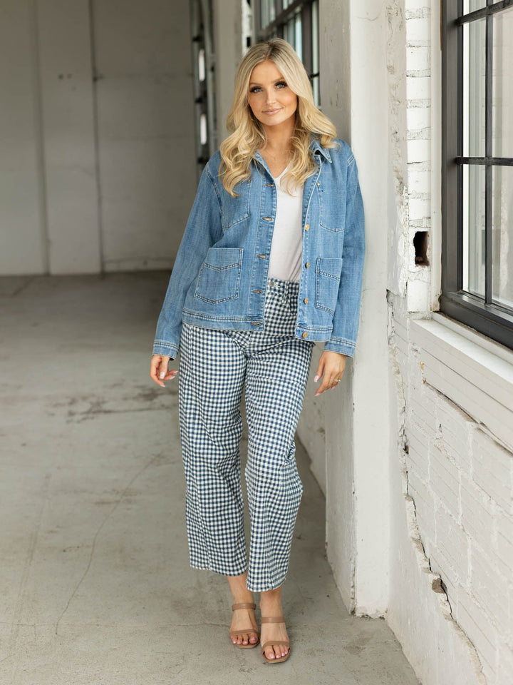 Woman wearing a denim jacket and checkered pants standing in an industrial-style room.
