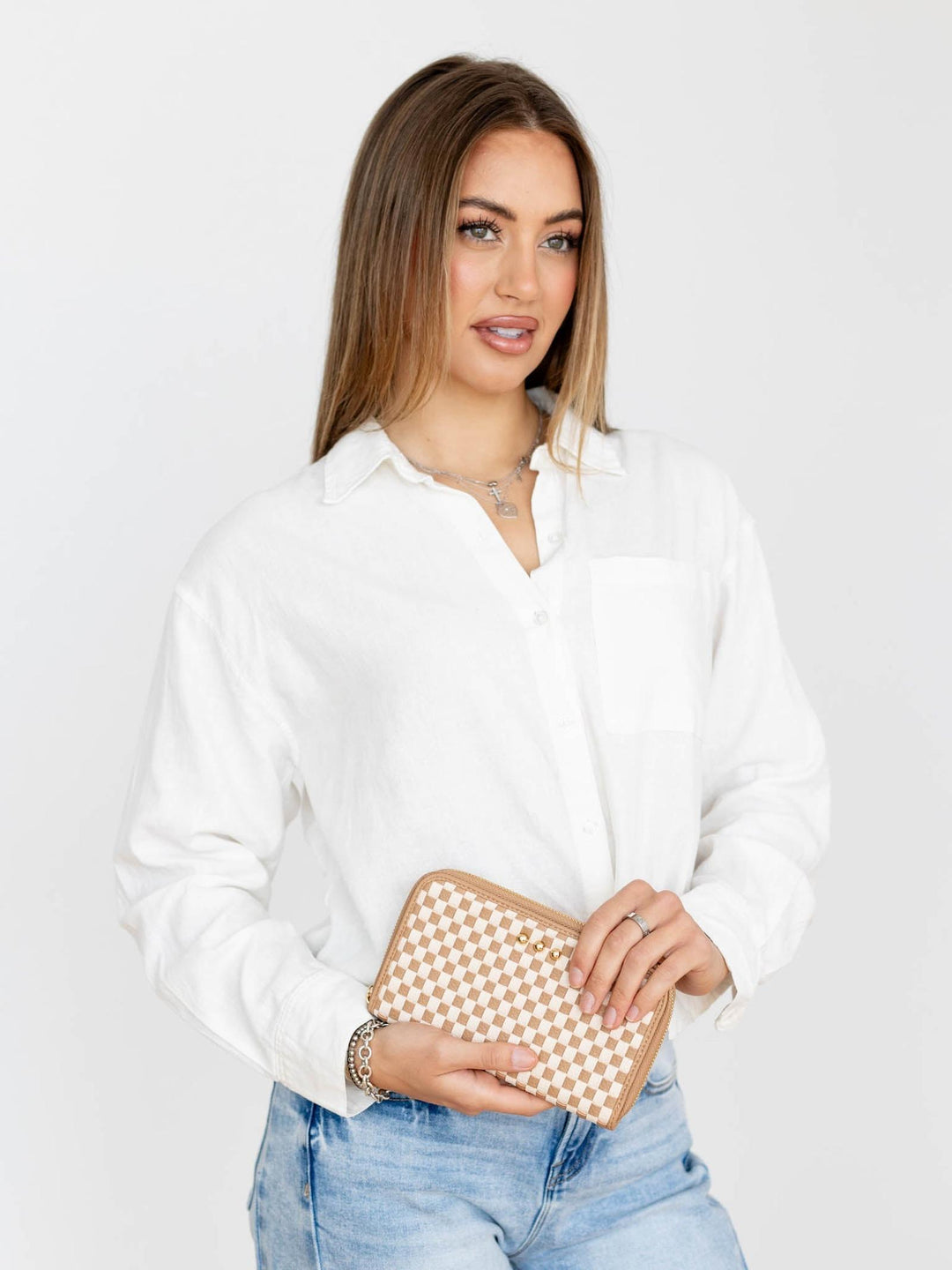Woman holding a beige clutch bag against a plain background