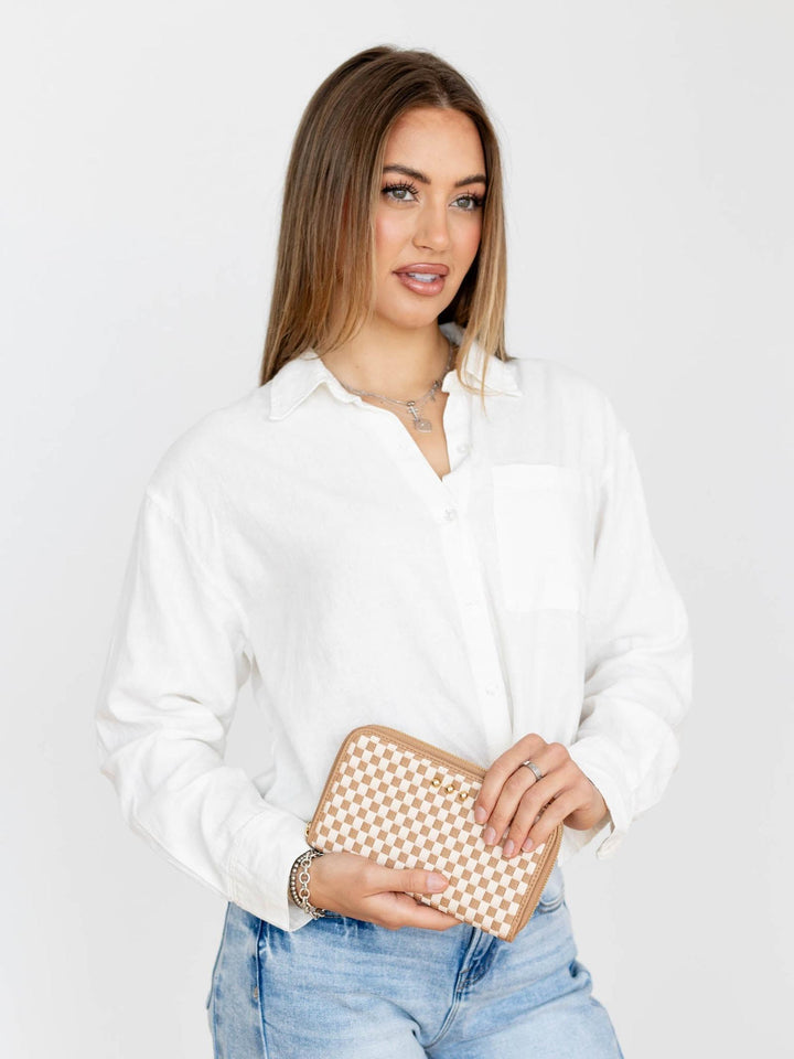 Woman holding a beige clutch bag against a plain background