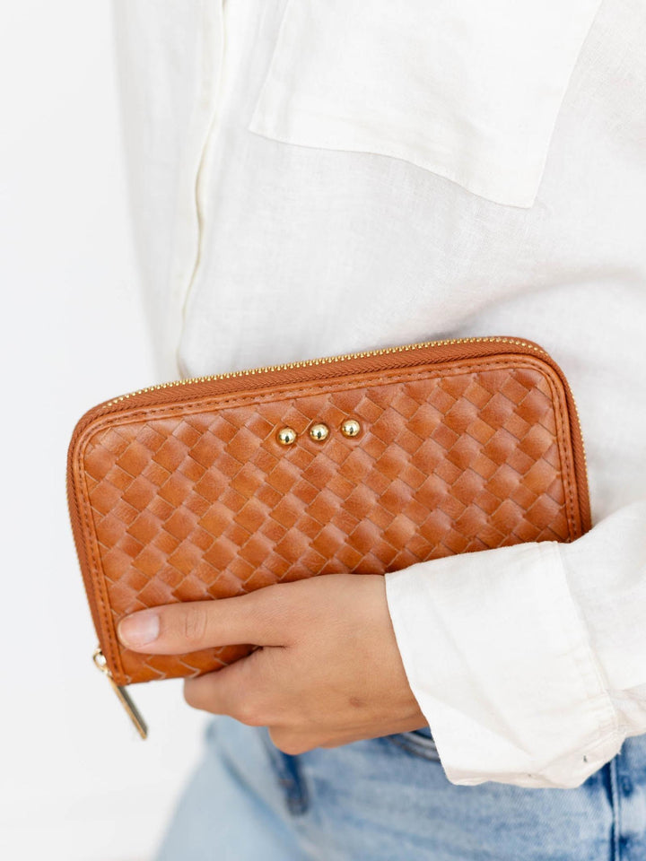 Person holding a brown woven wallet with a white shirt and blue jeans.
