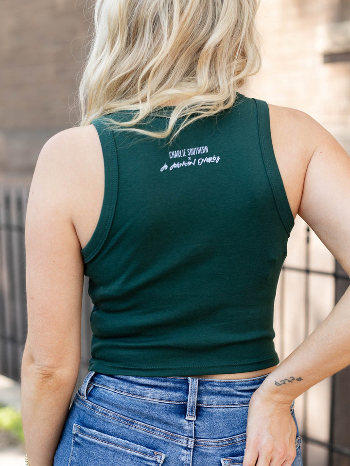 Woman wearing a green tank top with text, standing outdoors.