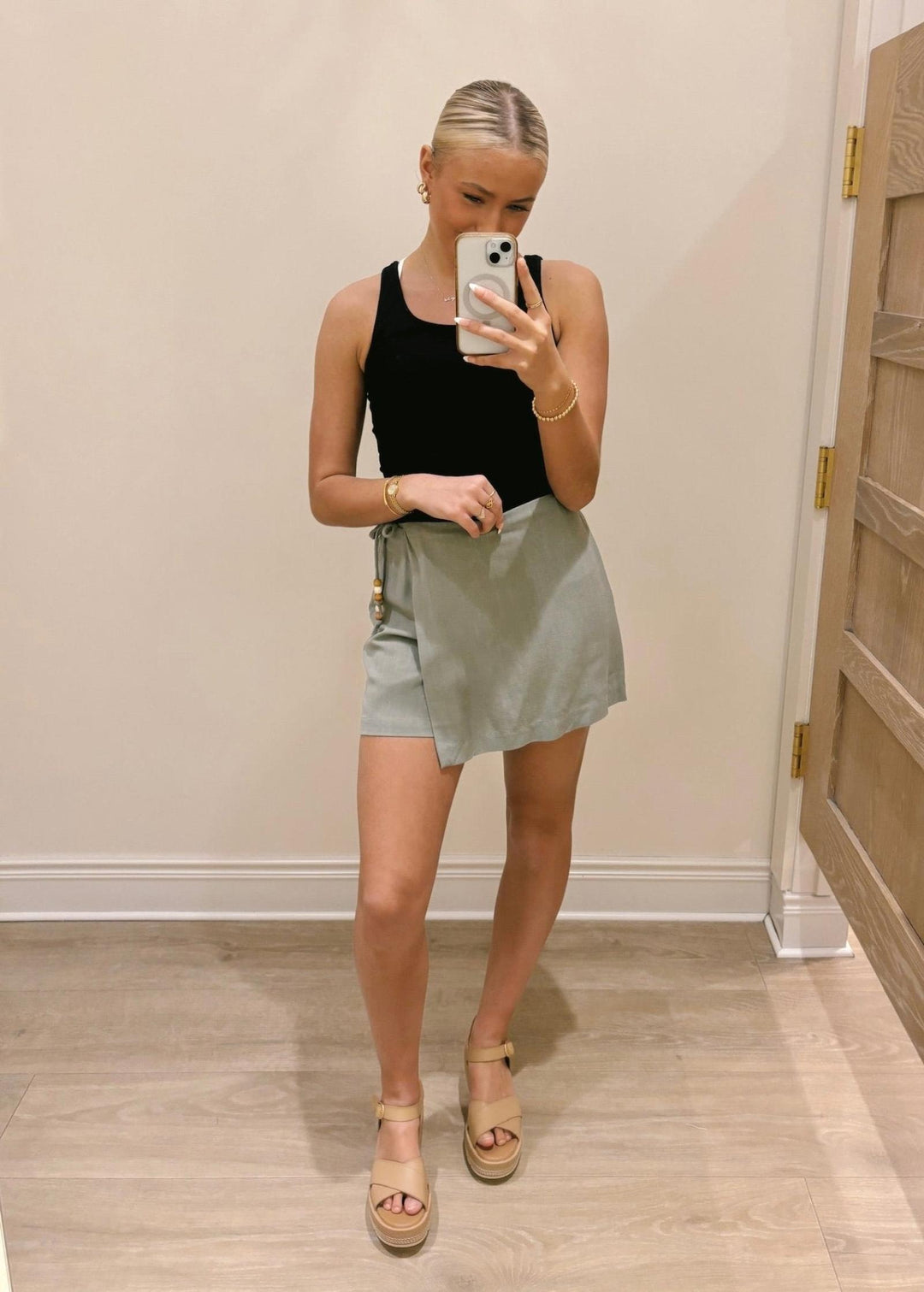 Woman taking a mirror selfie wearing a black tank top and light green skirt.